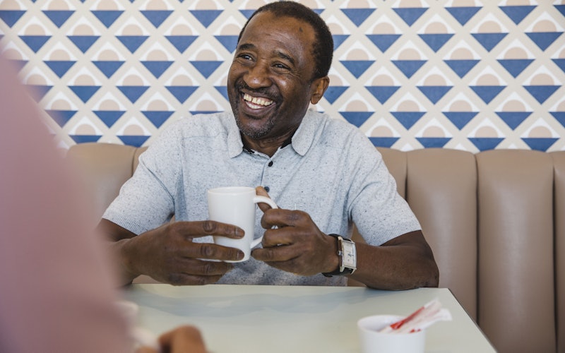 older man smiling in diner with coffee cup