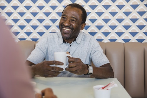 older man smiling in diner with coffee cup
