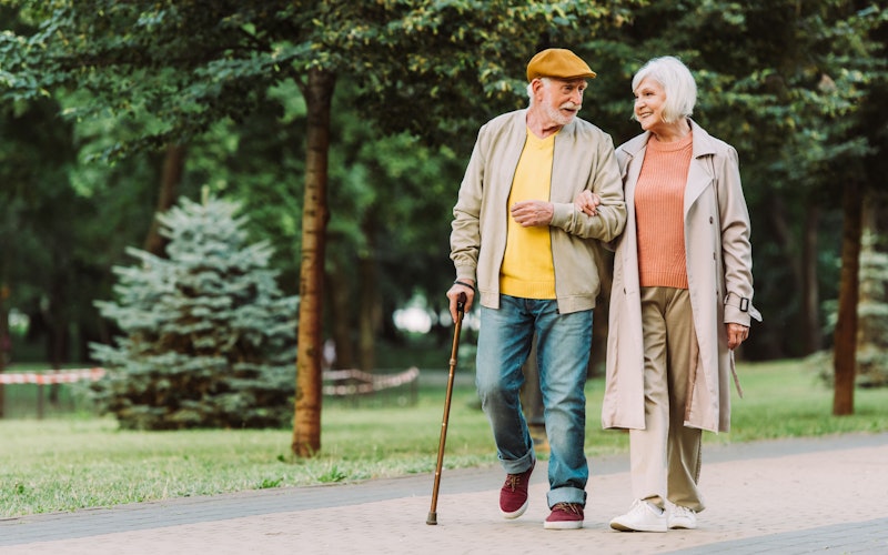 older couple walking on outdoor path with cane