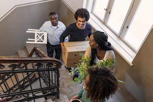 A family talking and smiling while moving items up a flight of stairs.