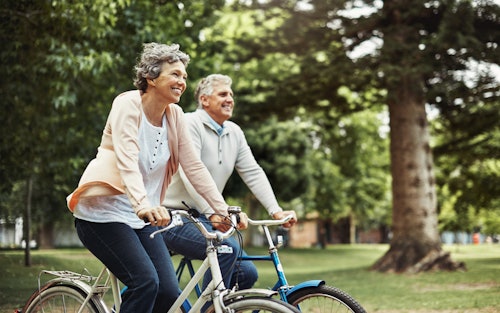 Elderly woman and man riding bikes outdoors.
