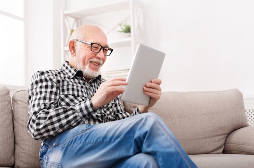 Senior sitting on couch reading tablet