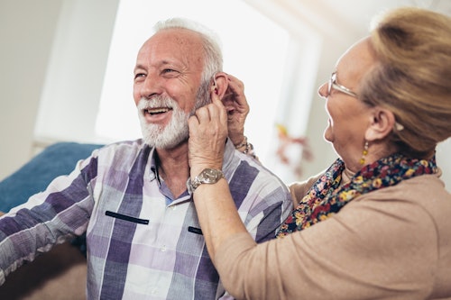Woman helping her husband to fit his hearing aid