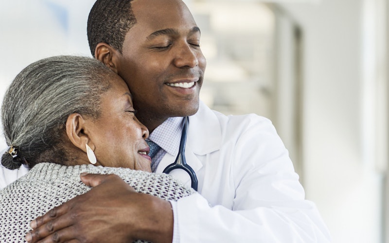 An older adult embraces a doctor, who has his hand on the patients back.