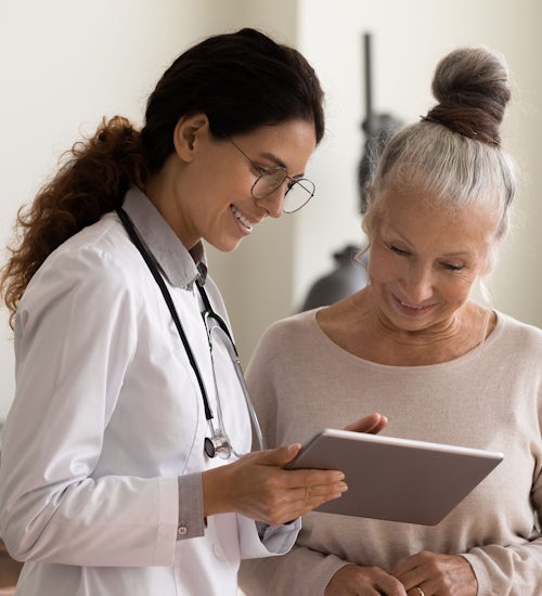 A doctor holds and points to a tablet while both she and a patient look at the device.