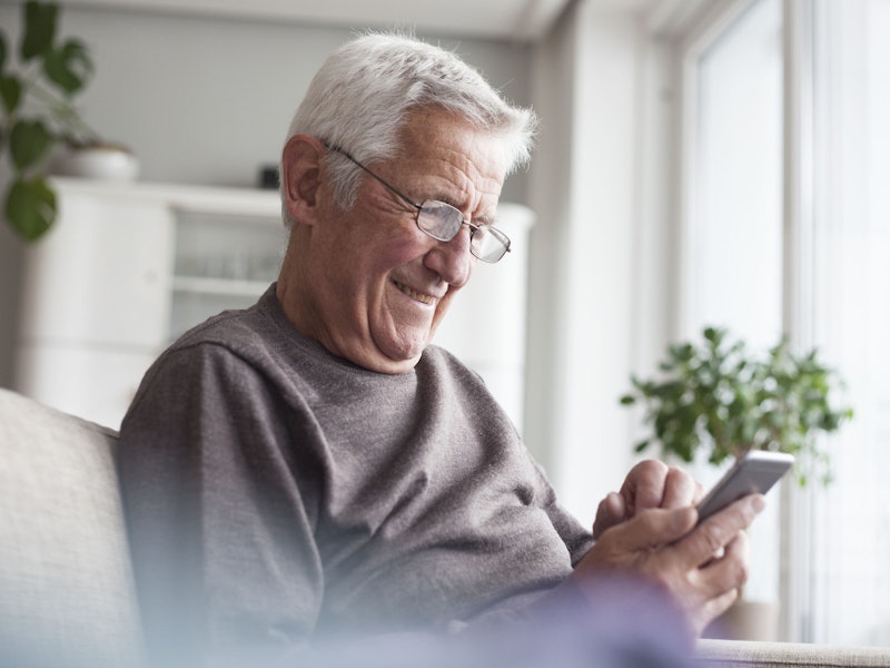 An older adult smiling while looking at the phone they are holding.