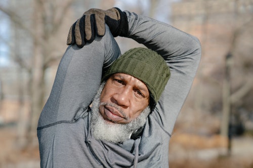 Elderly black man stretching his right shoulder in an autumn park.