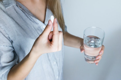 woman holding half-full glass and white medicine pill