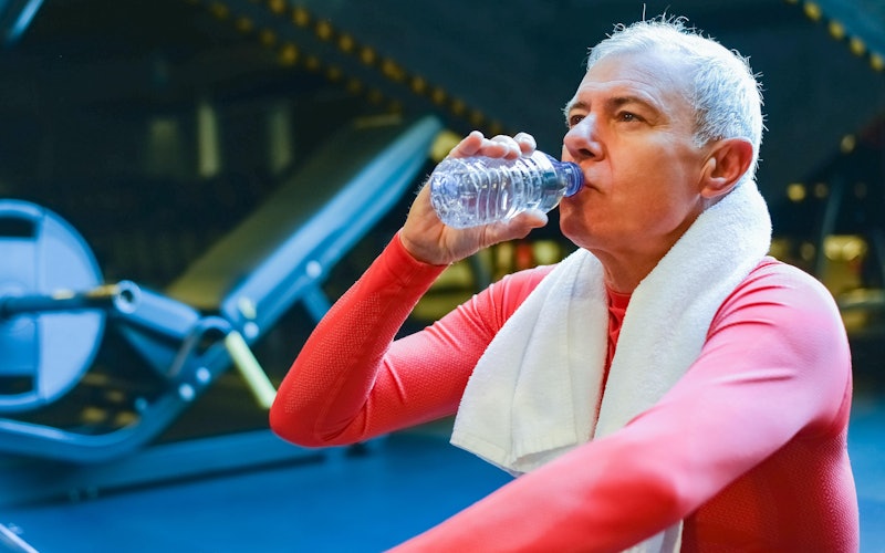 older man drinking water bottle in gym
