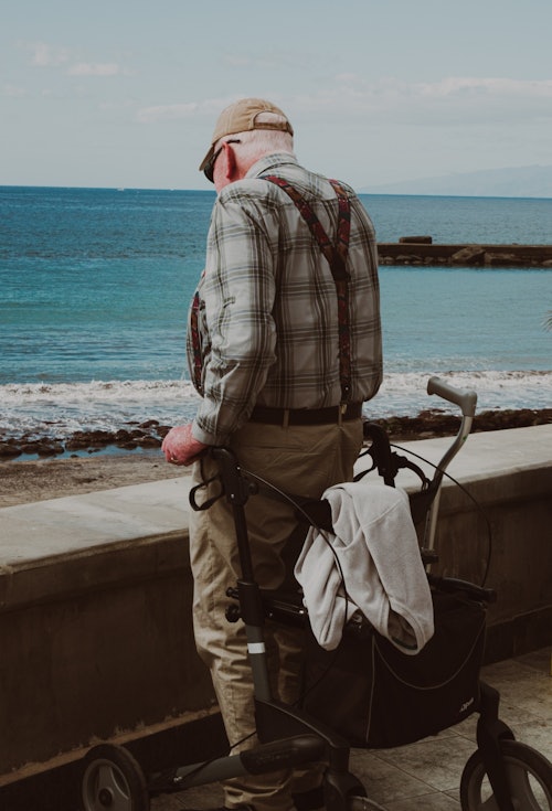 old man standing by walker and ocean