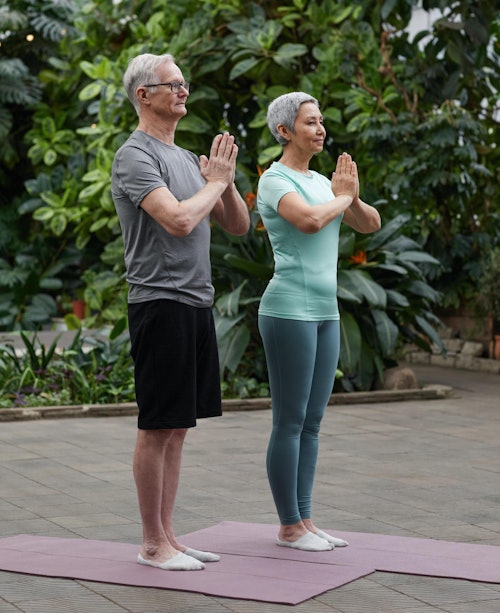 Older couple standing on yoga mats outside