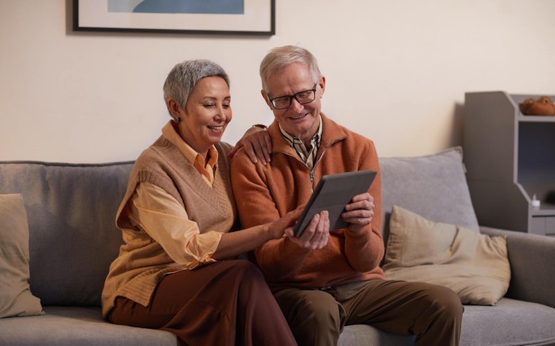 A couple sitting side by side on a sofa and looking at a tablet.