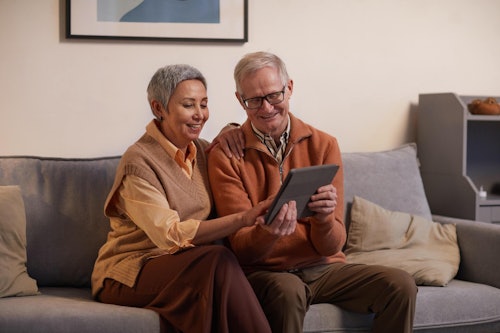 A couple sitting side by side on a sofa and looking at a tablet.