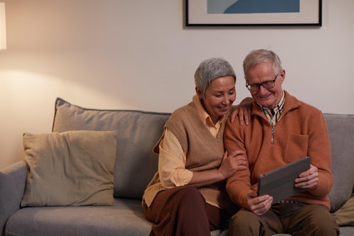 Man and woman sitting on sofa while looking at a tablet computer.