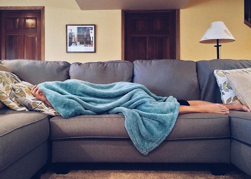 person lying on couch covered by a blanket