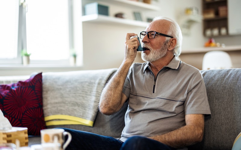 Older man using an asthma inhaler at home