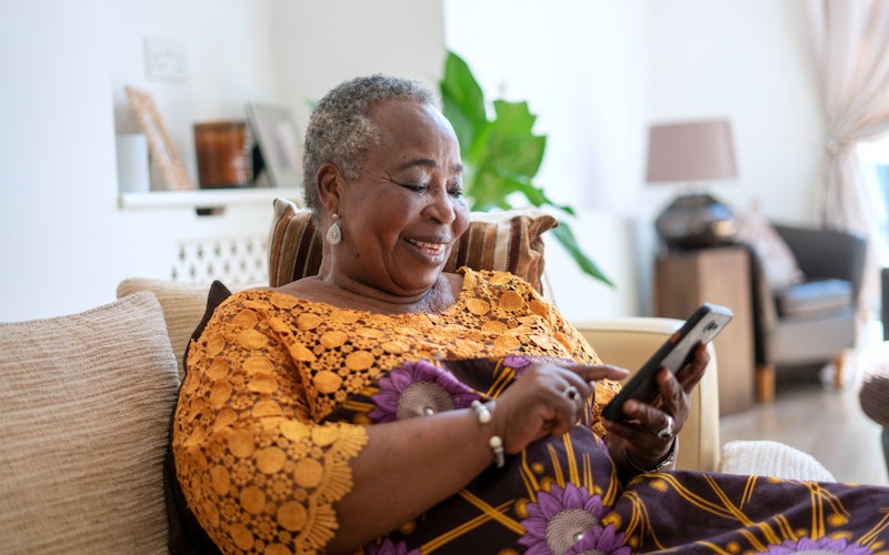 Mature woman sitting on the couch and using her cell phone