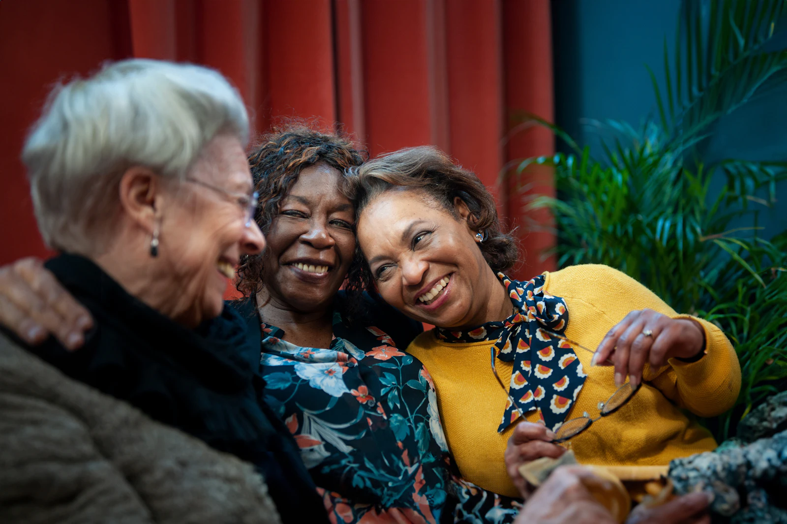 Women hugging in front of red curtain and plant