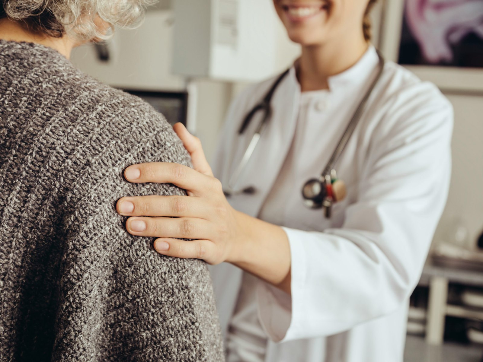Close up of a doctor's hand on a patient's shoulder while the two stand face to face.