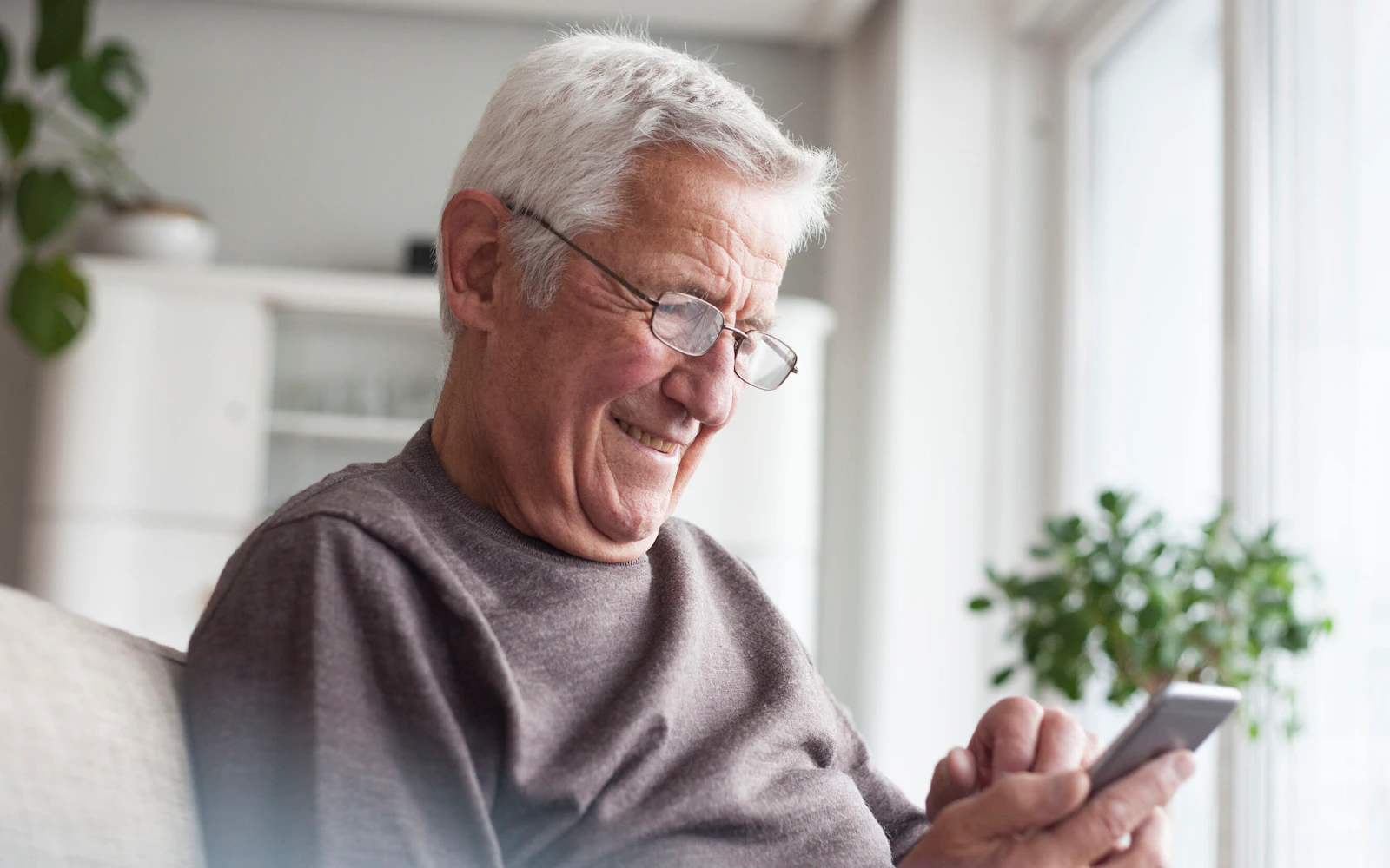 An older adult smiling while looking at the phone they are holding.
