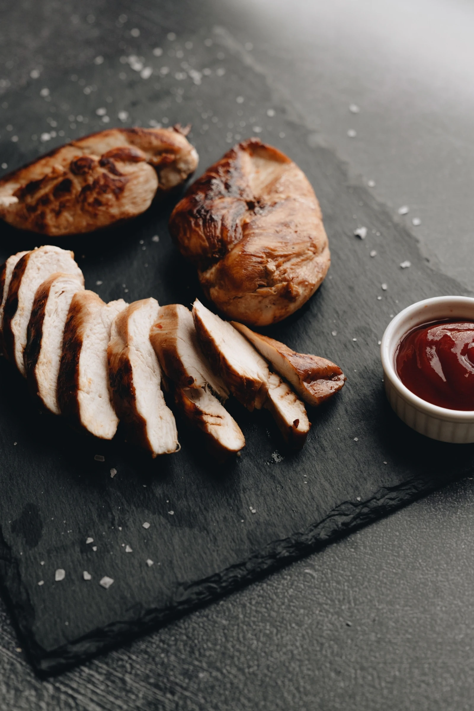 Sliced grilled chicken breast barbecue sauce in white cup black slate background