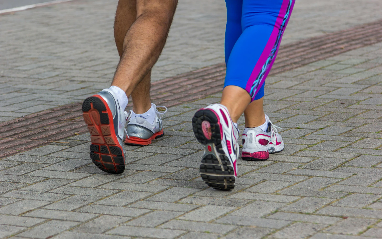 close up of man and woman wearing sneakers running pavement