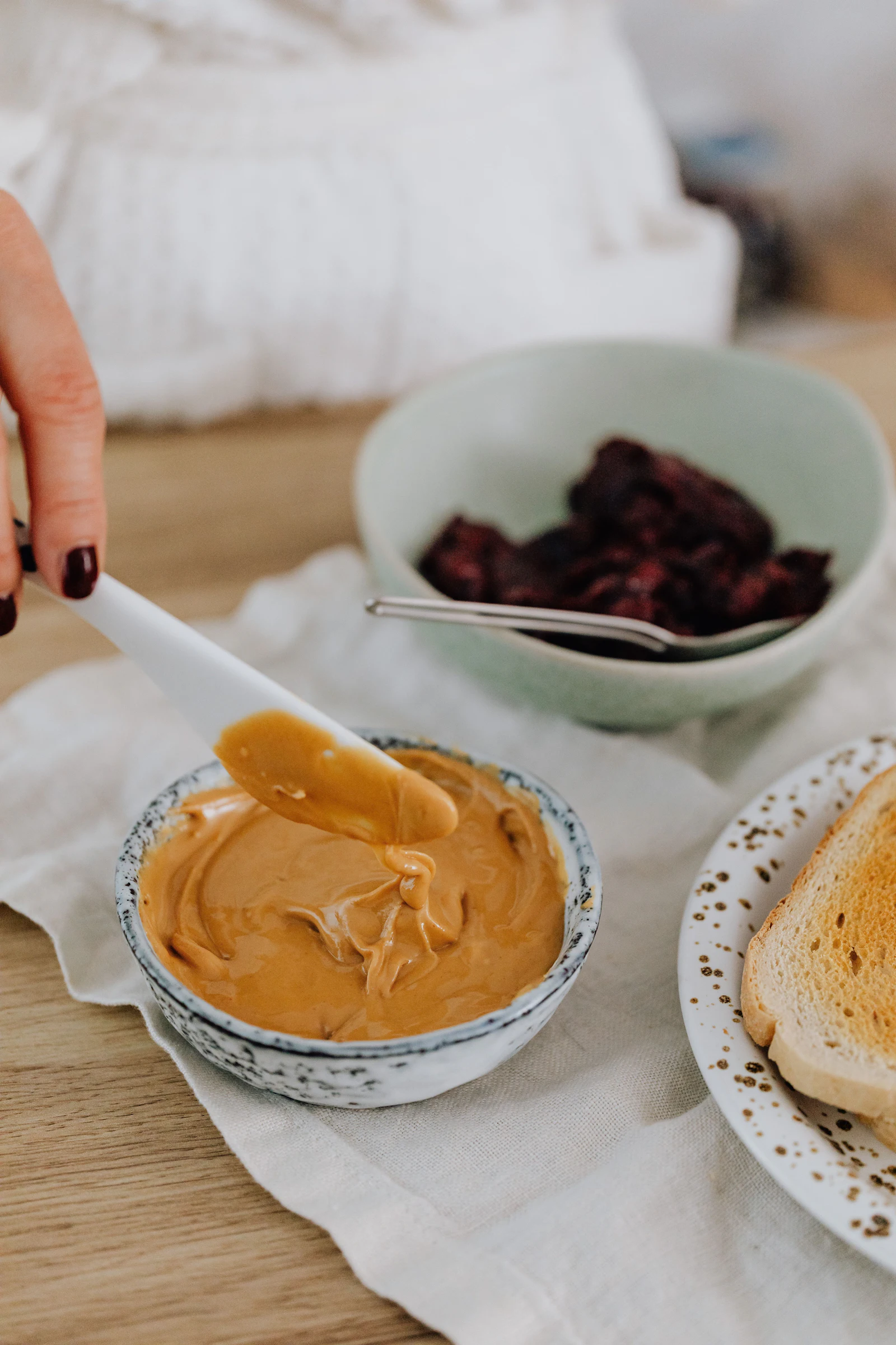 Peanut butter spread, berries, toast, ceramic bowls, wood table, white placemat