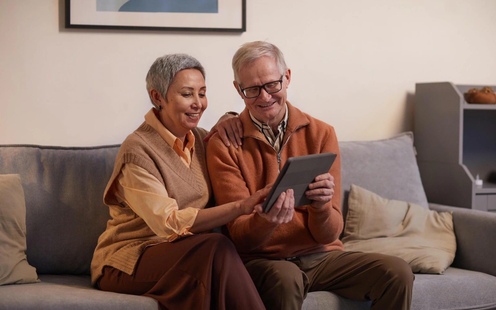 A couple sitting side by side on a sofa and looking at a tablet.