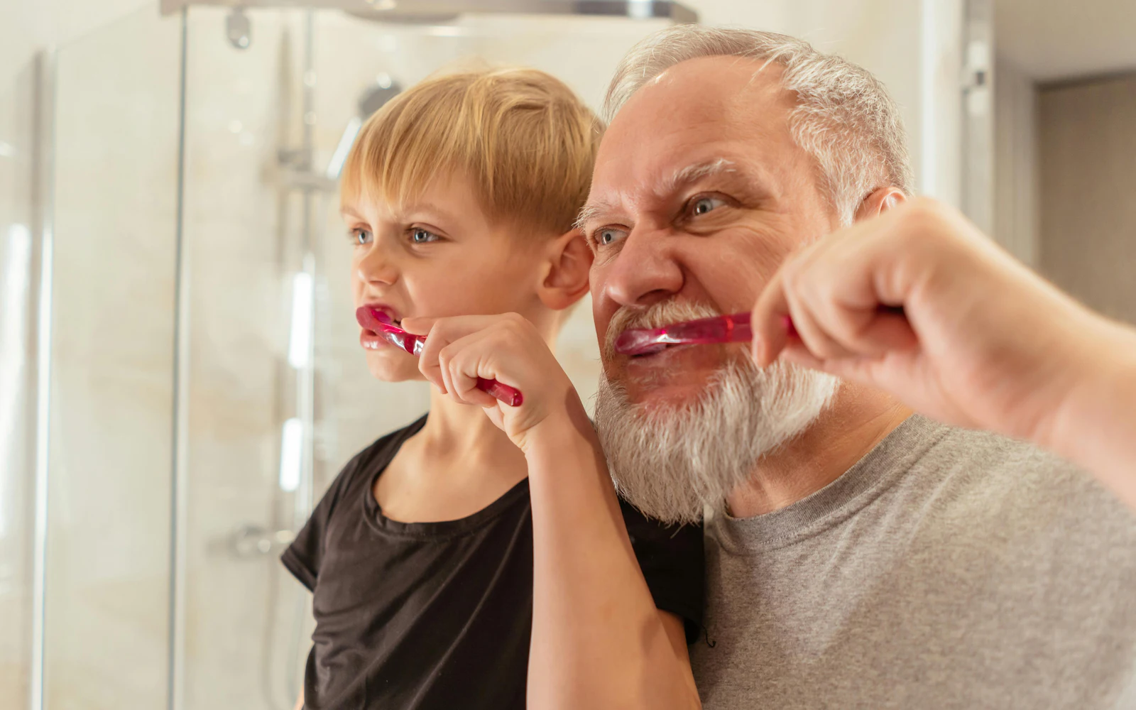Senior brushing teeth alongside his grandson