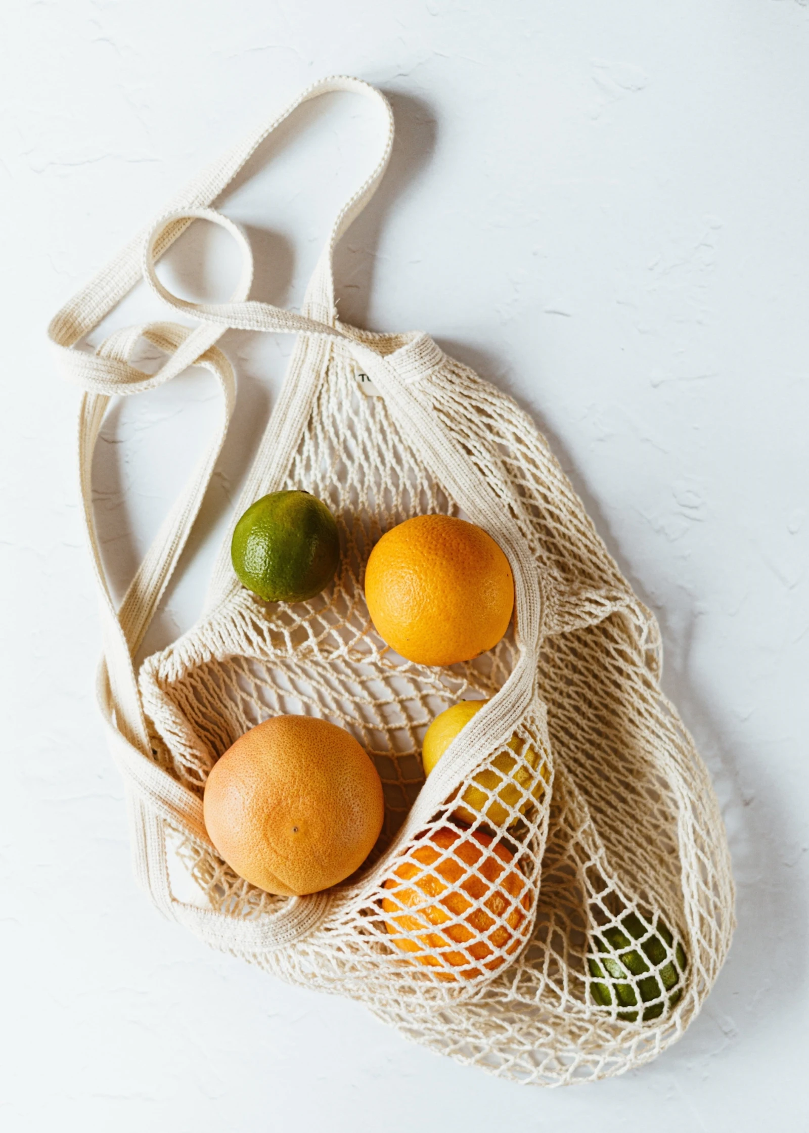 assorted citrus fruits in a cotton sack on a white surface
